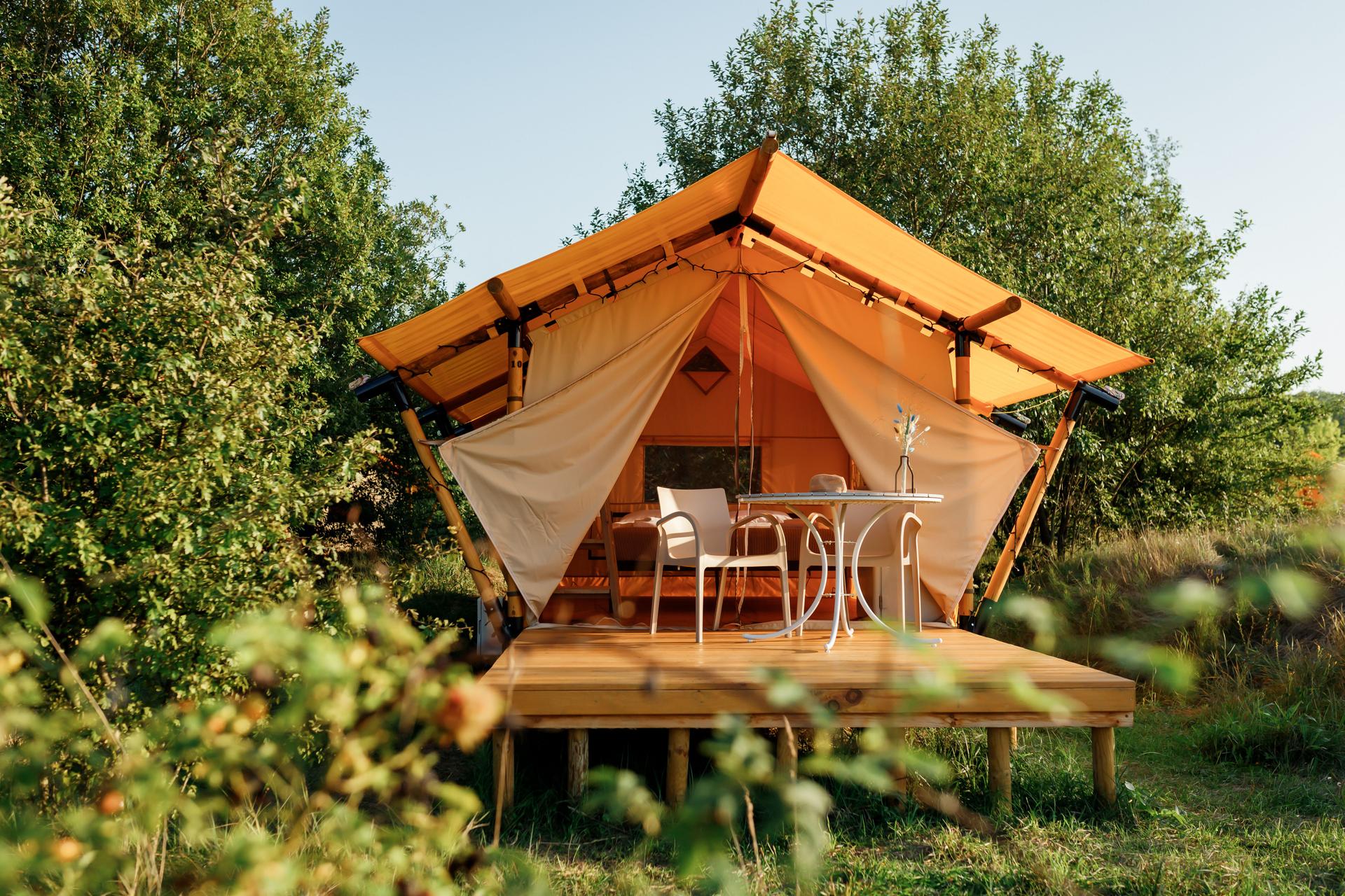 Cozy open glamping tent with light inside during sunset. Luxury camping tent for outdoor summer holiday and vacation. Lifestyle concept