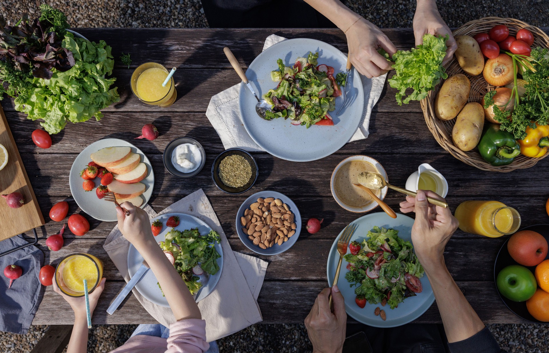 Father mother and daughter eating fresh vegetable salad with fresh vegetables, tomatoes, bell pepper, potato, fruits and dipping sauces on wooden desk at outdoor garden, Conceptual of party family healthy