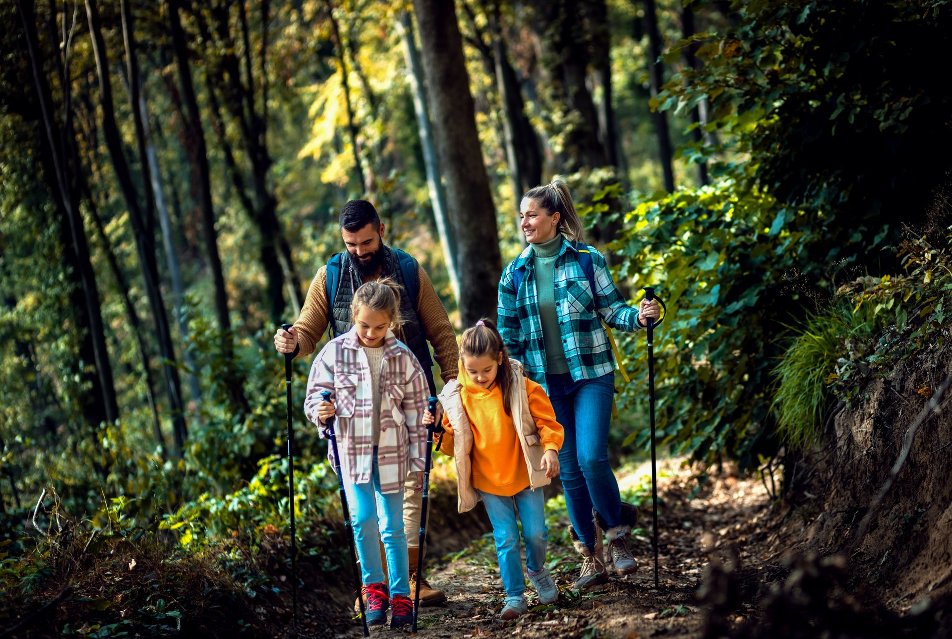 Smiling family of four enjoying hiking in trough forest.